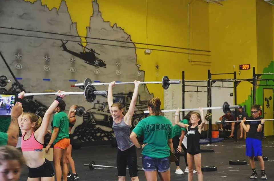 Athletes pressing barbells overhead with judges in matching shirts