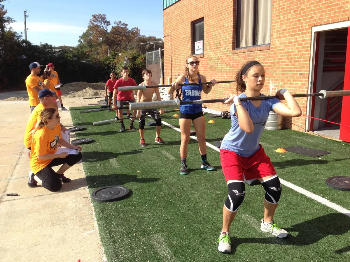 Athletes performing barbell squats outdoors with judges scoring