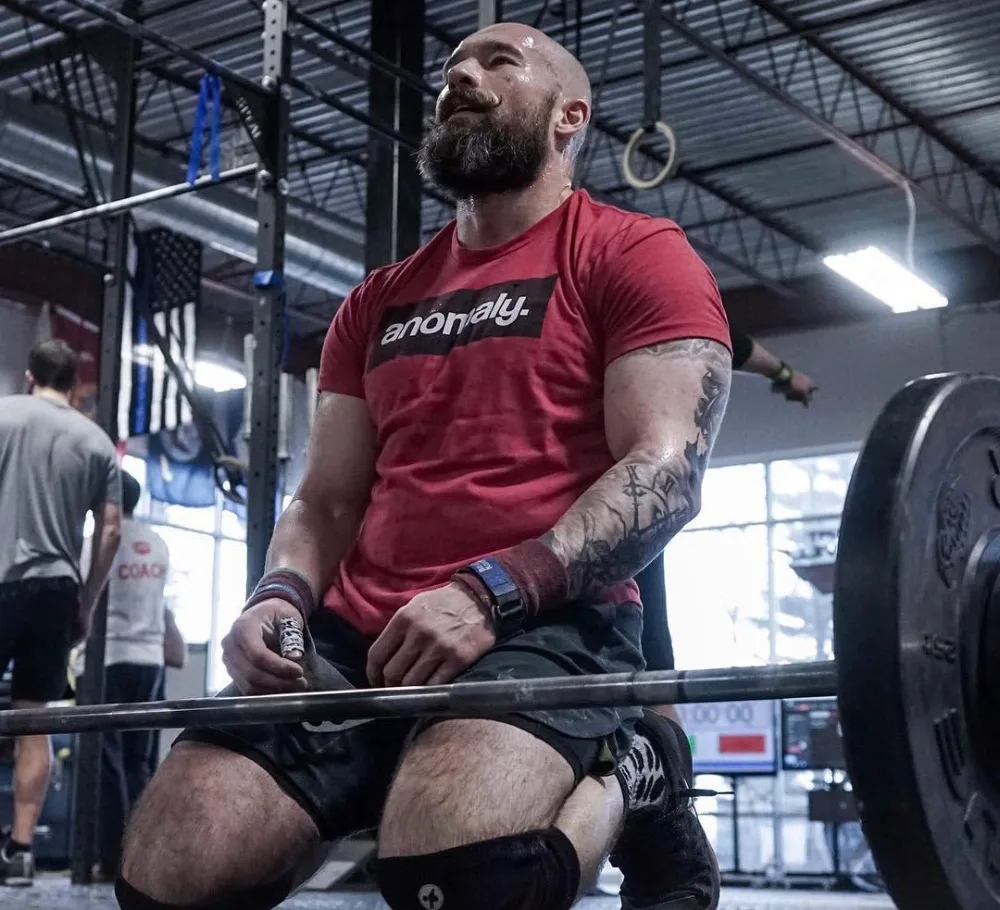 A masters athlete catching his breath, kneeling at the barbell