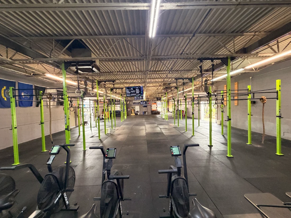 The competition floor at CrossFit Gallant — green Rogue rigs down both sides with rowers and bikes staged for the event